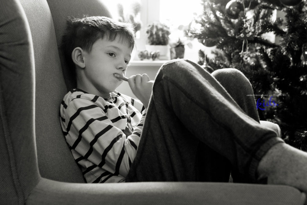 boy cleaning his teeth in armchair in living room with Christmas tree on background