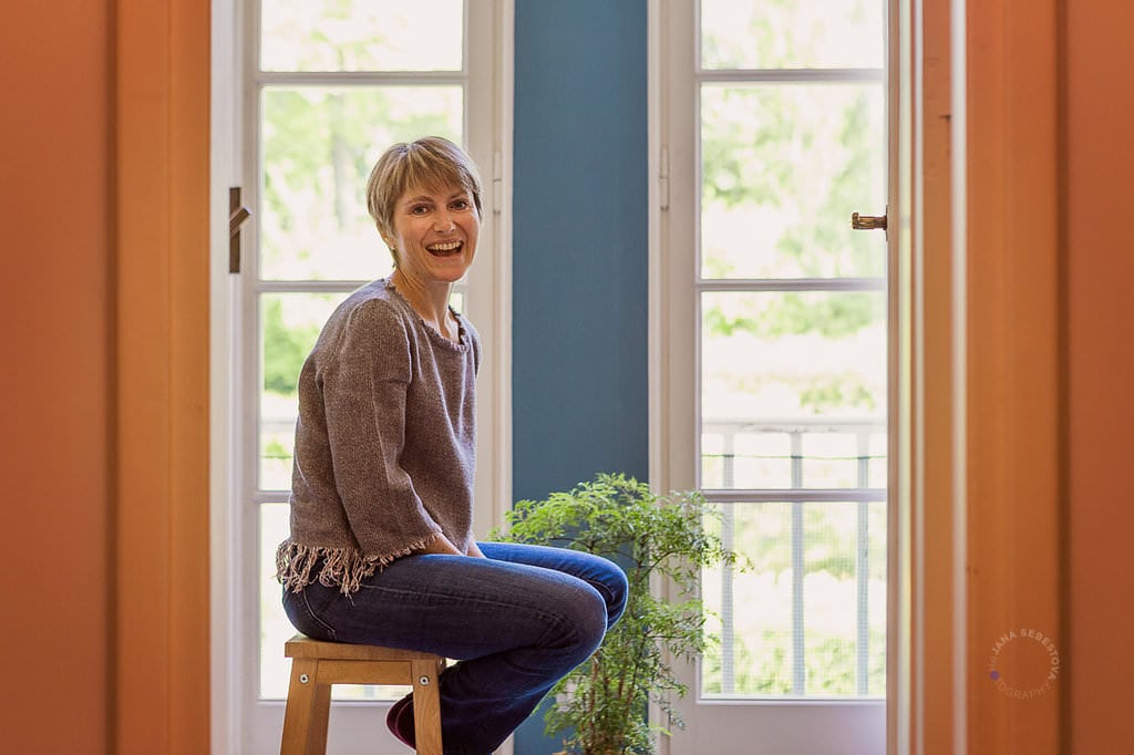 a woman sitting in front of symetric windows on high chair smiling