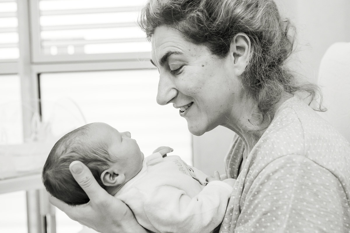 servizio fotografico neonato - mamma sorride al suo bebe neonato sul letto in ospedale