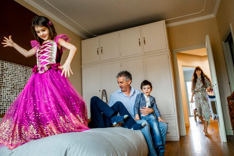 famiglia in camera da letto con mamma che arriva e bimba vestita da principessa che balla sul lettone