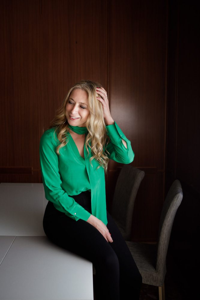 donna in camicia elegante verde seduta sul tavola di aggiusta i capelli