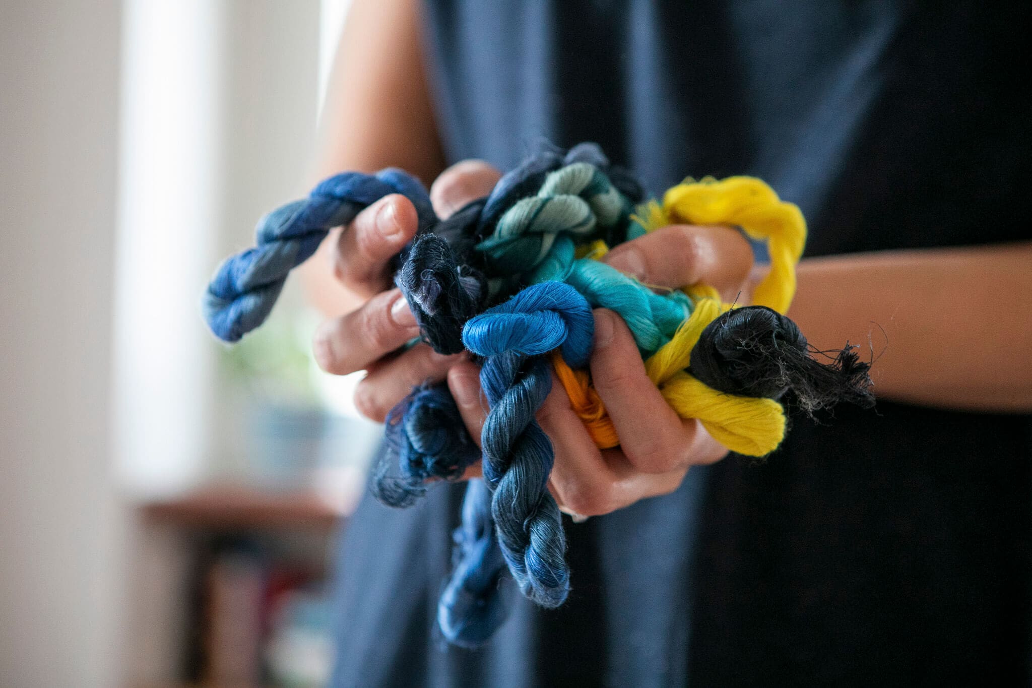 dettaglio mani che tengono trecce di filati colorati