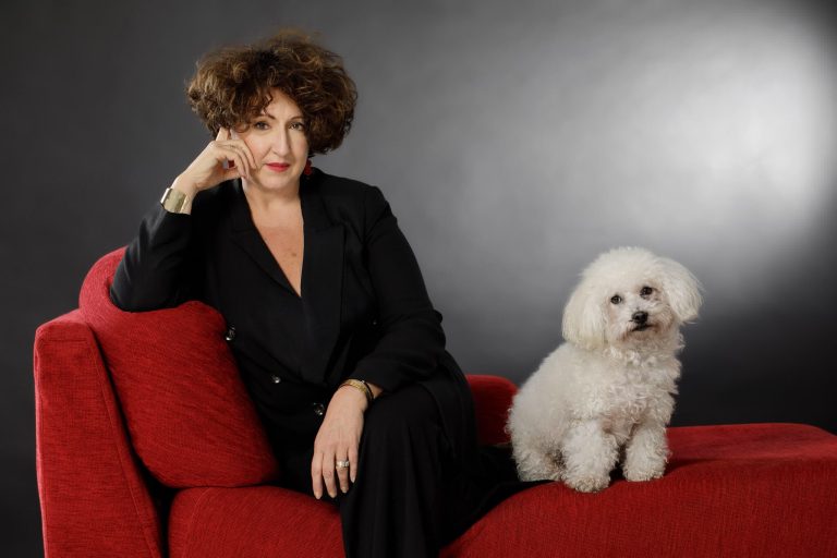 avvocata con capelli ricci seduta su divano rosso con suo cane bianco di fianco
