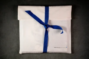 A white fabric pouch tied with a blue ribbon, designed for storing a special photo book. A white fabric pouch tied with a blue ribbon, designed for storing a special family or portrait photo album