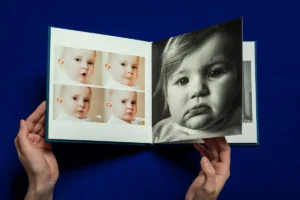 A person opening a photo album with images of a baby, including a large close-up. A person opening a photo album with images of a baby, including a large close-up.