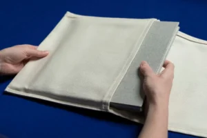 A person carefully placing a fabric-covered book into a protective sleeve. A person carefully placing a fabric-covered family album into a protective sleeve.