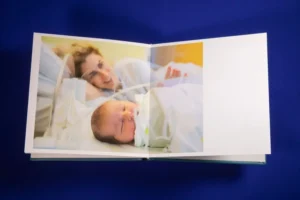 A photo book open to an image of a mother and newborn baby in a hospital setting. A family album open to an image of a mother and newborn baby in a hospital setting.