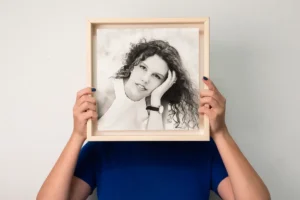 A person holding a framed black-and-white portrait of a curly-haired woman. A person holding a framed black-and-white portrait of a curly-haired woman.