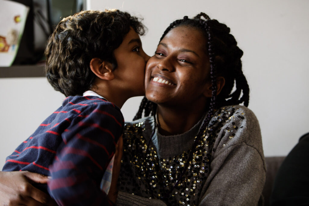 black woman smiling while kissed by her son