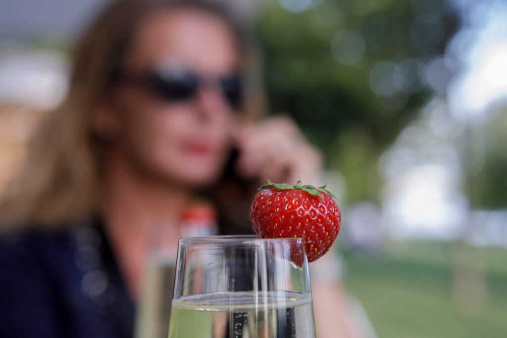 blurred portrait of woman on telephone outside in bar with glass with prosecco and strawberry in front