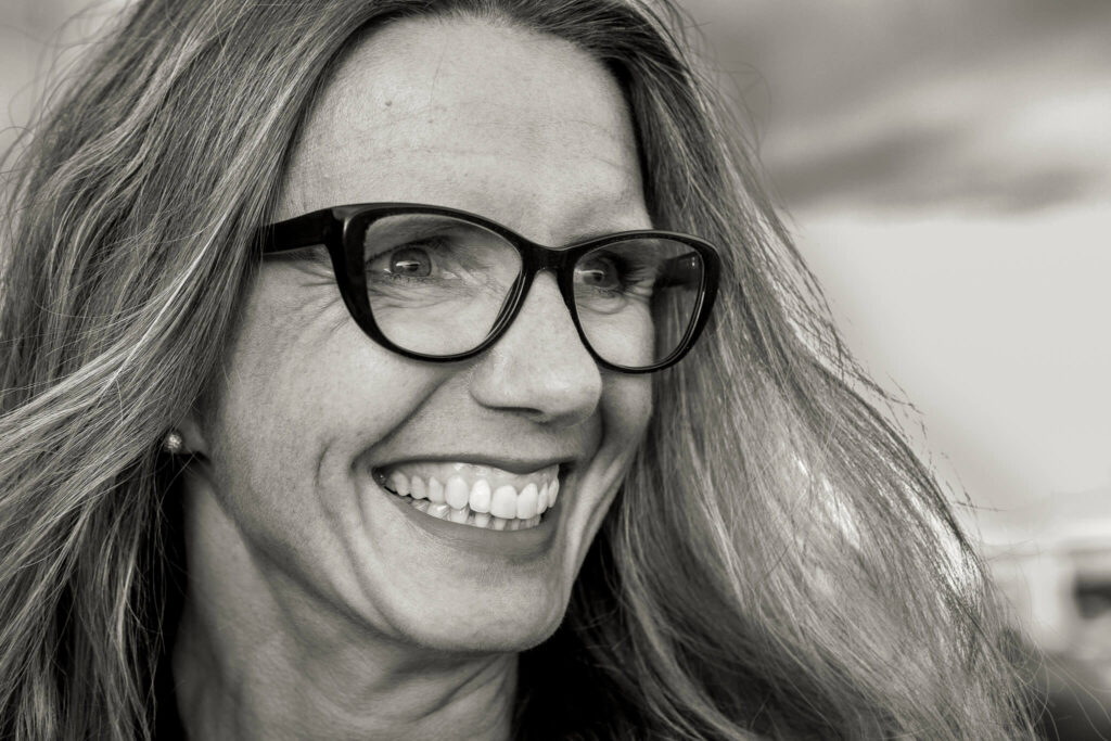 close-up black-and-white portrait of woman with glasses and open smile looking sidewards