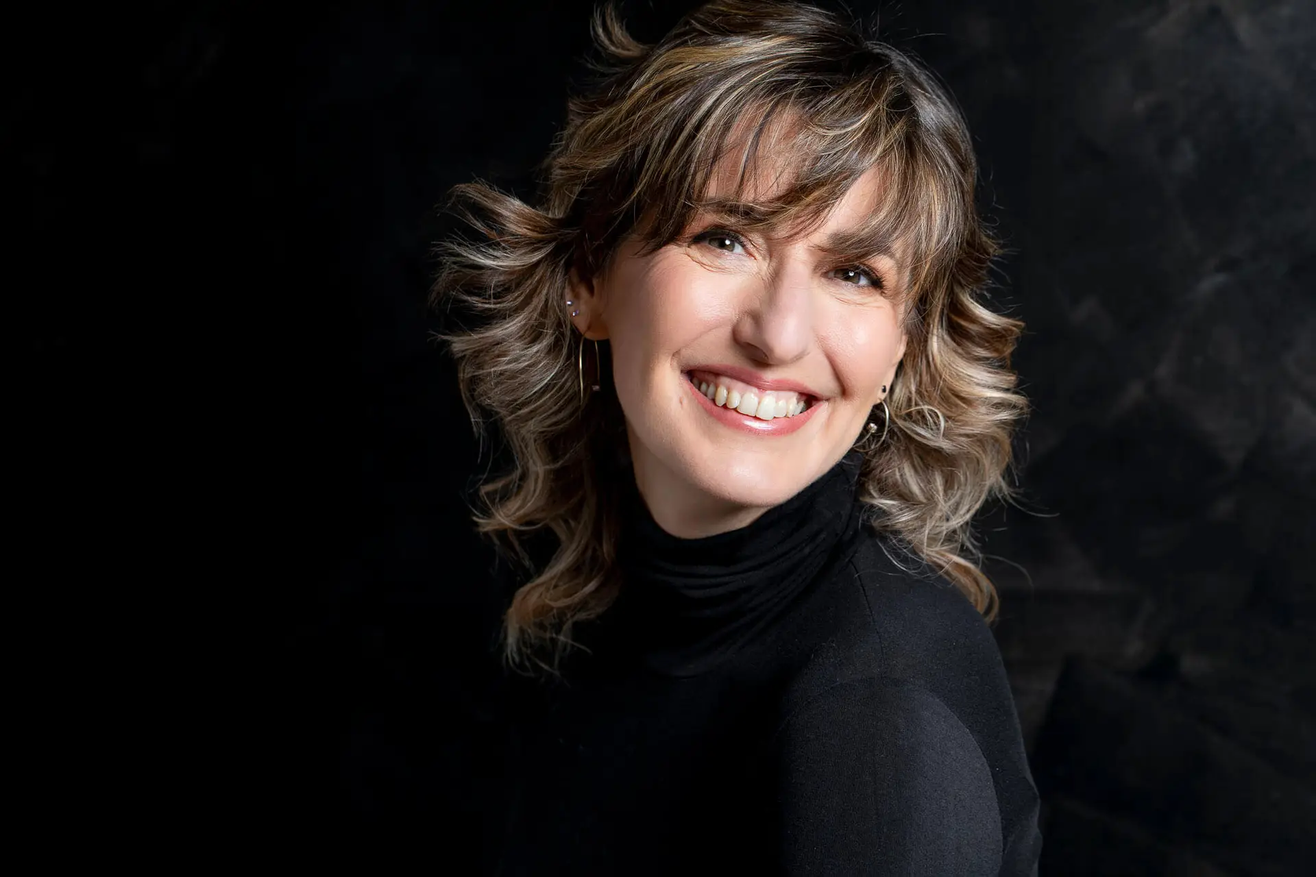 primo piano sullo sfondo nero di donna vestita di nero con grande sorriso e testa inclinata